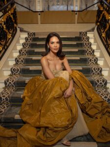 Esha Gupta seated on stairs in a regal gold couture outfit.